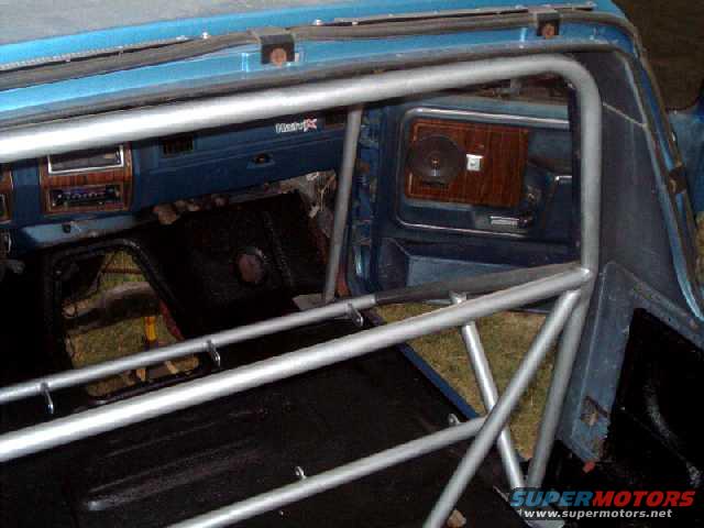 Interior of a blue vehicle with a metal roll cage, wood-grain trim, and black flooring