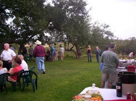 People gathered outside under trees at a party with food laid out on tables
