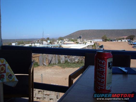 view of boats parked in a dry, dusty area with a hill in the background. A can of Tecate sits on a table in the foreground