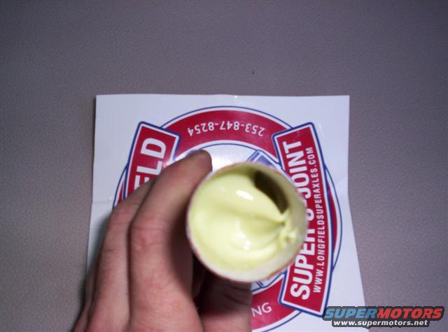 Hand holding a tube of yellow grease over a sticker that says "LONGFIELD SUPERJOINT" and "WWW.LONGFIELD SUPERAXLES.COM"