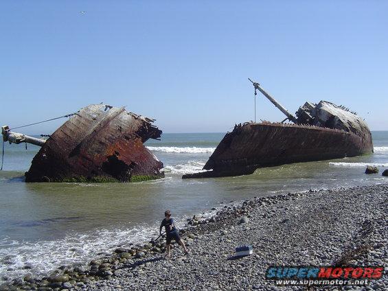 Broken shipwreck on a rocky beach with a person standing nearby