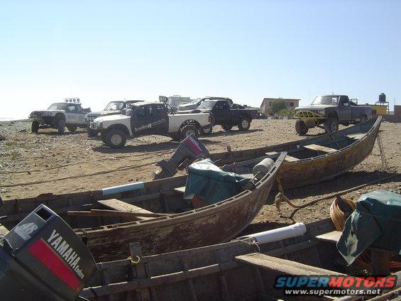 Several pickup trucks parked on a beach near fishing boats