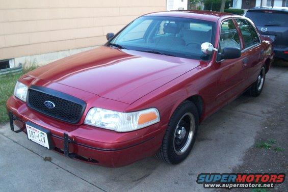 Red Ford Crown Victoria parked outside a building, with a dark SUV behind it. License plate is visible