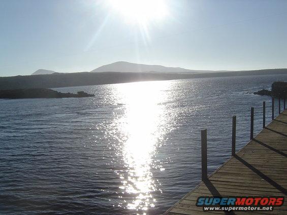 Water reflecting sun, wooden dock, distant hills
