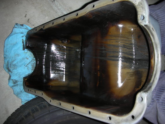 Inside of a dirty oil pan with dark sludge and oil residue