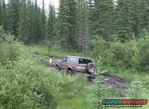 Brown Ford Bronco driving on a muddy forest trail