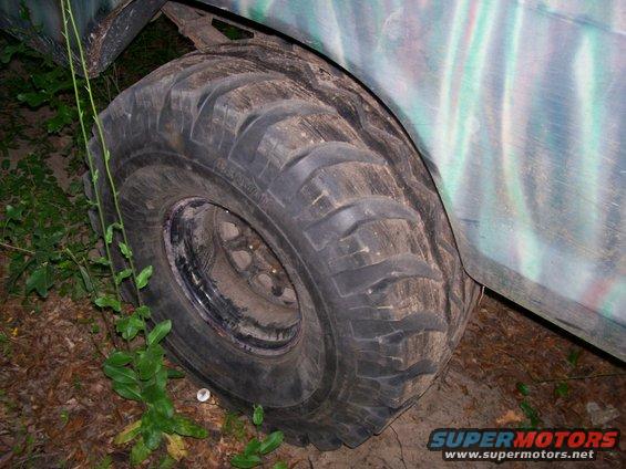 Close-up of a large off-road tire on a vehicle, with camouflage paint on the body