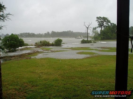 Flooded area with choppy water, trees, and a distant boat. Overcast sky