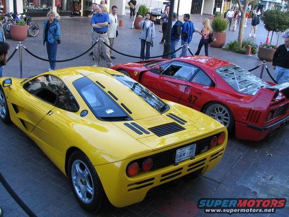 Yellow sports car rear view, black stripes on engine cover, round taillights, license plate visible