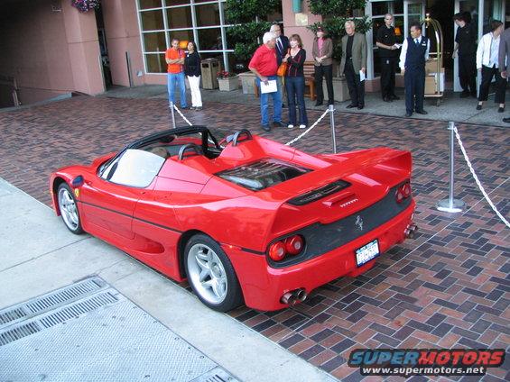 Red convertible sports car parked on brick pavement, rear view. License plate visible
