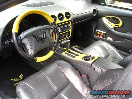 Car interior with black leather seats, yellow accents on the steering wheel and dashboard, and a bird emblem on the steering wheel