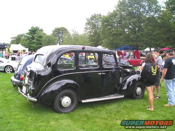 Black sedan with suicide doors and exposed engine, parked on grass at an outdoor event