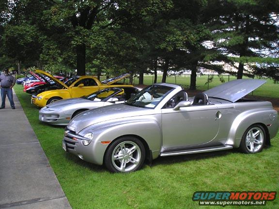Several cars parked on grass with hoods and trunks open. One silver convertible is in the foreground