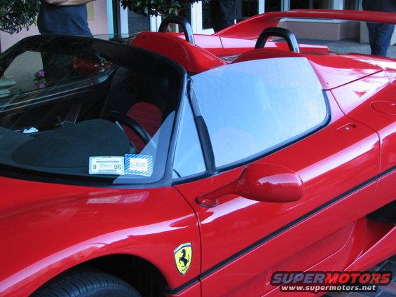 Red convertible sports car with black interior, yellow Ferrari badge on fender, and a sticker on the windshield