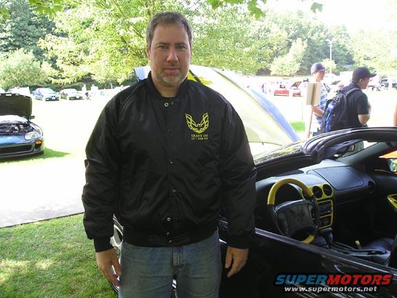 Black convertible interior with yellow accents, man in Trans Am jacket, other cars in background