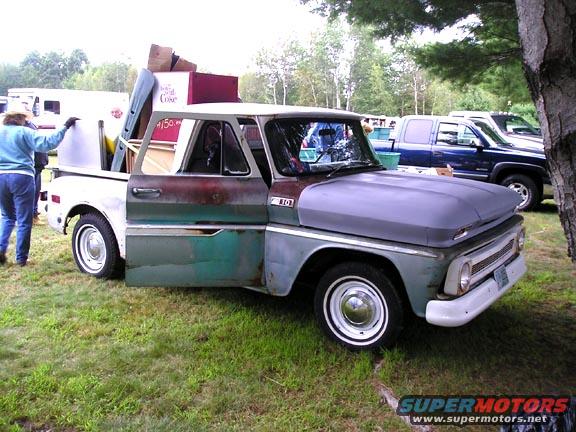 Old pickup truck with its door open, loaded with boxes and household items. A blue pickup truck is parked behind it