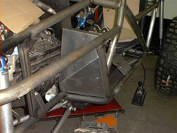 Off-road vehicle roll cage structure with engine components and a large tire visible
