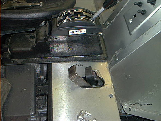 Interior shot of a vehicle's center console area, showing a shifter and a brake lever. There's some handwritten text on a metal plate