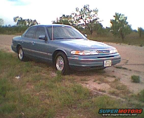 Blue 1995 Ford Crown Victoria sedan parked on grassy shoulder, front 3/4 view