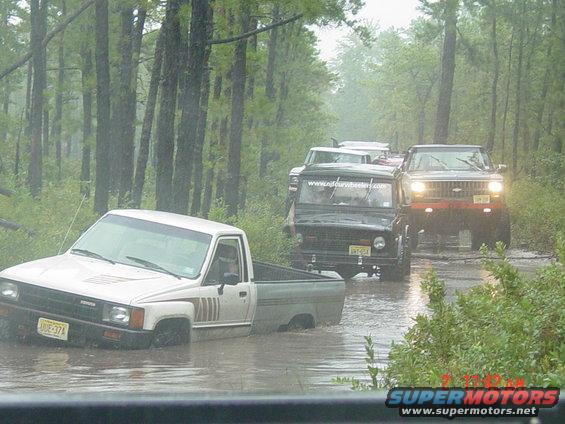 Toyota pickup truck stuck in water, with other off-road vehicles behind it on a dirt road