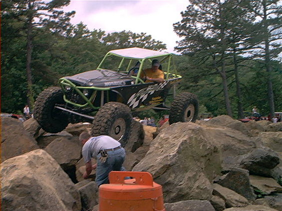 Buggy with roll cage climbing over rocks, driver in yellow shirt
