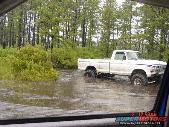 White pickup truck with lifted suspension driving through flooded area near trees