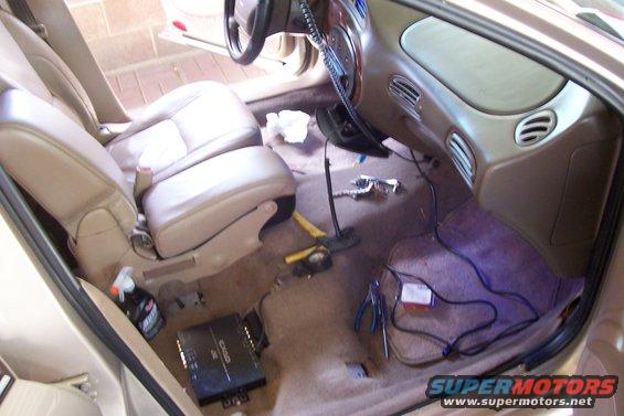 Car interior showing front seats, dashboard, and floor with tools and audio amplifier