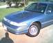 1994 Ford Crown Victoria - A blue sedan is parked on a paved surface with grass and trees in the background.