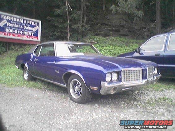 Blue 1972 Oldsmobile Cutlass Supreme coupe with a silver roof, parked next to a dark blue SUV