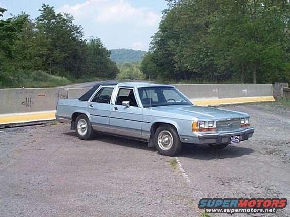 1991 Ford Crown Victoria sedan parked on a dirt road next to a concrete barrier