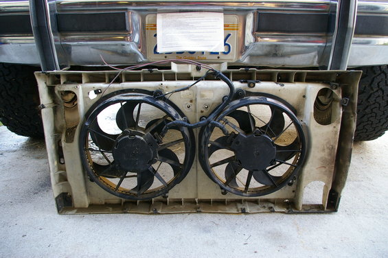 dual electric fans mounted in a plastic shroud, with part of a truck bumper and tire visible behind
