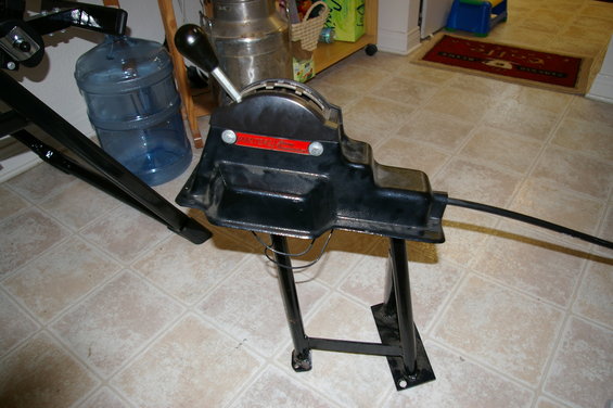 Black shifter assembly with red label, mounted on metal stand. Water cooler in background