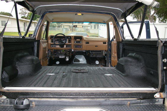 Brown dashboard and black spray-lined cargo area of an older Ford Bronco, viewed from the rear