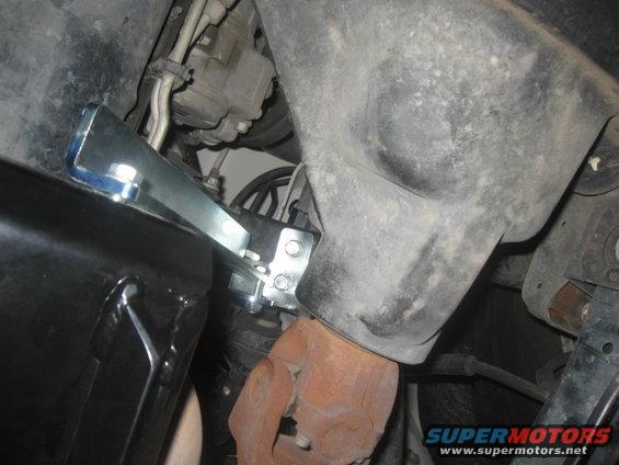 Underside of a vehicle showing a rusty exhaust pipe connected to a bracket, with a black component to the left