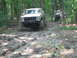 1992 Ford Mustang - A white 1979 Ford Bronco navigates a muddy trail in a wooded area, with another vehicle visible in the background.