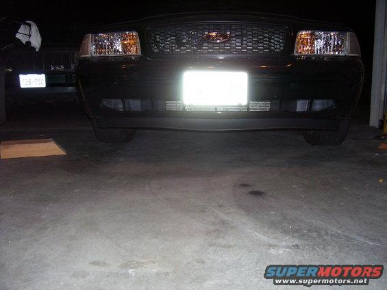 2002 Ford Crown Victoria front end with grille and headlights visible. Another vehicle is parked to the left