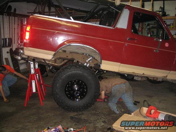 Red 1990 Ford Bronco on jack stands, undergoing repairs in a garage