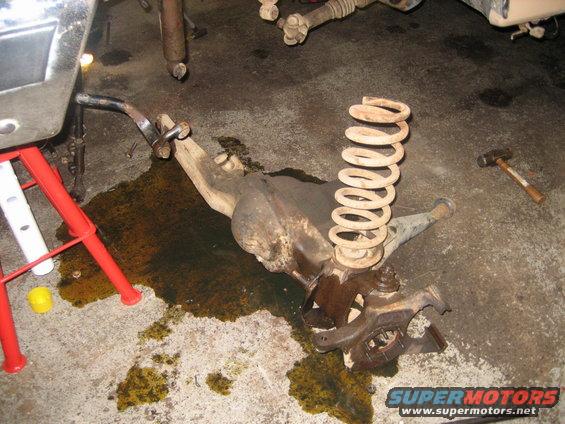 Suspension parts and a coil spring lie on a concrete floor with oil stains