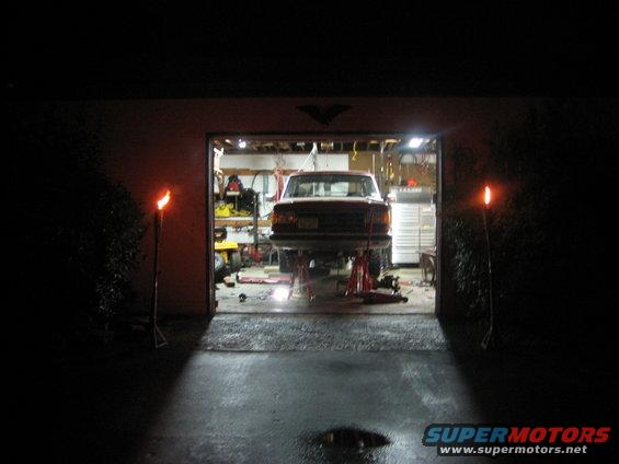 Red 1990 Ford Bronco on jack stands in garage, rear view