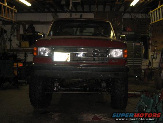 Red Ford Bronco with lifted suspension and large tires, viewed from the front in a garage