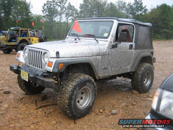 Silver 2002 Jeep Wrangler covered in mud, parked off-road with other Jeeps visible