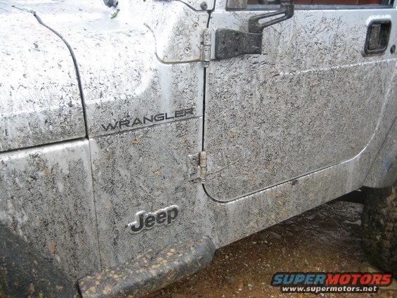Side of a muddy Jeep Wrangler with 'Jeep' and 'Wrangler' badges visible