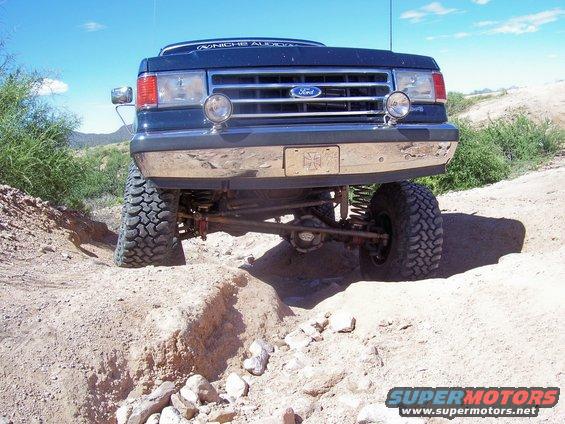 Dark blue 1992 Ford Bronco with lifted suspension driving on a dirt trail, front view