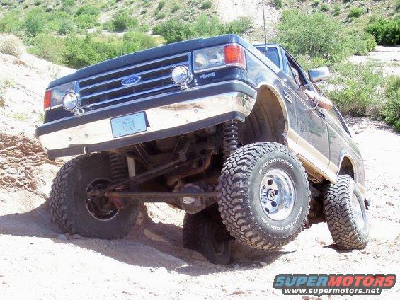 Ford Bronco with lifted suspension driving on a dirt hill. Front grille shows Ford logo
