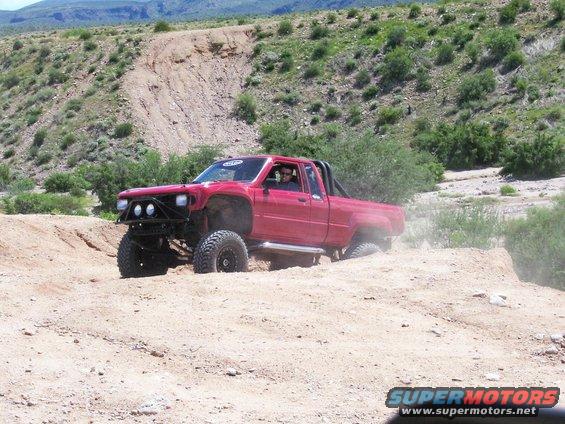 Red pickup truck with off-road modifications navigating sandy terrain