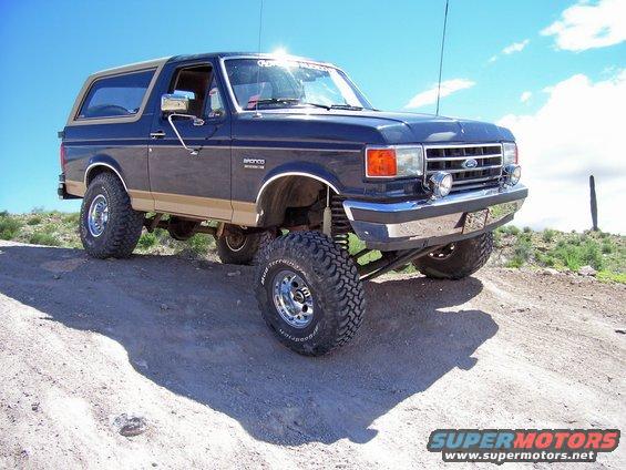 Lifted 1991 Ford Bronco, dark blue with tan trim, on dirt road