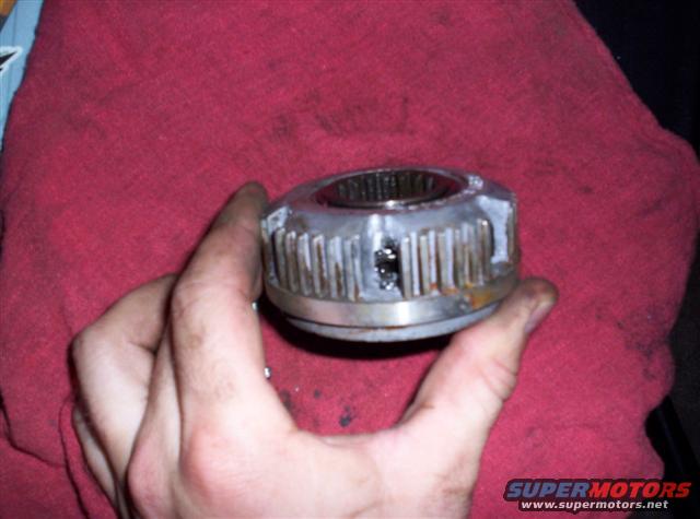 Metal U-joint part held in hand over red cloth, showing splines and damage