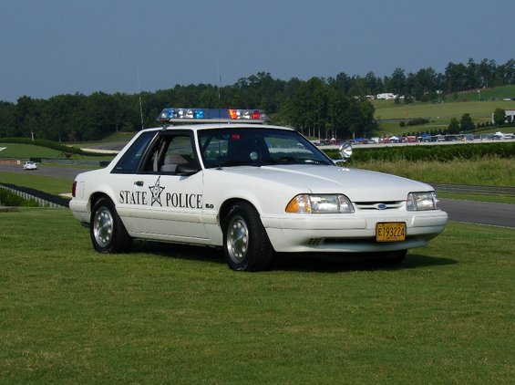 White 1993 Ford Mustang police car with "STATE POLICE" text and light bar, parked on grass