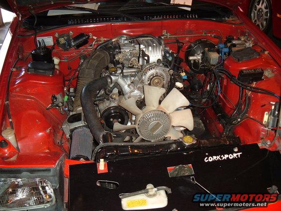 Engine bay with a rotary engine, fan, and radiator. Black cover has "CORKSPORT" text
