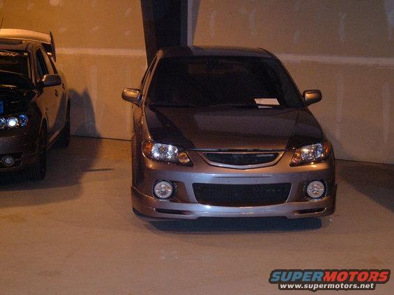 Front view of a modified car with aftermarket bumper and headlights. Another car is partially visible to the left